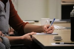 Person writing with left hand and blue biro pen on table