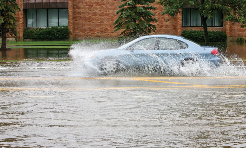 Car driving through a large puddle on a flooded urban road, spraying water