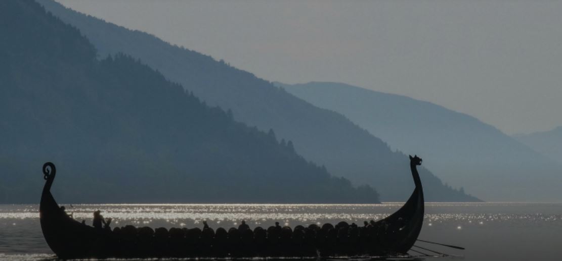 Viking boat in silhouette on water against mountain backdrop