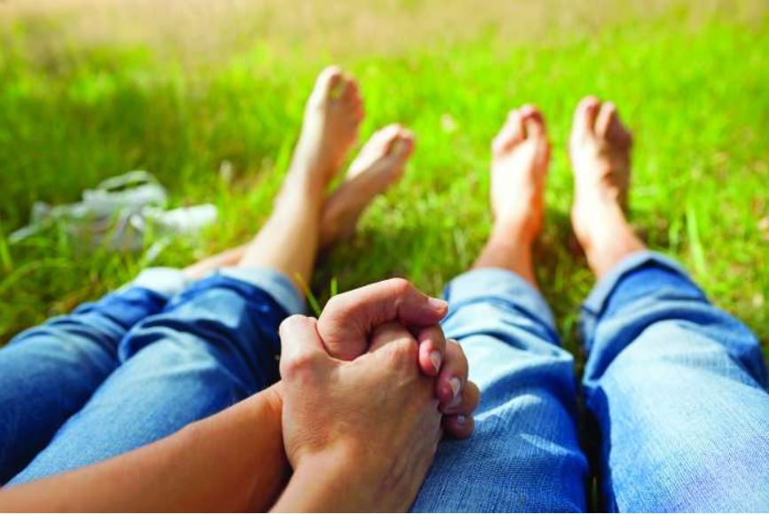 View of two people clasping hands between their thights with outstretched legs and bare feet