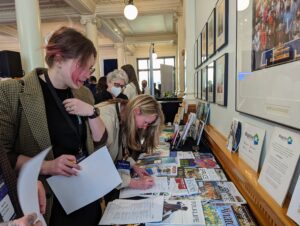 Showcase attendees view table displaying MagsBC member magazines at the BC Legislature Hall of Honour, May 18/22.