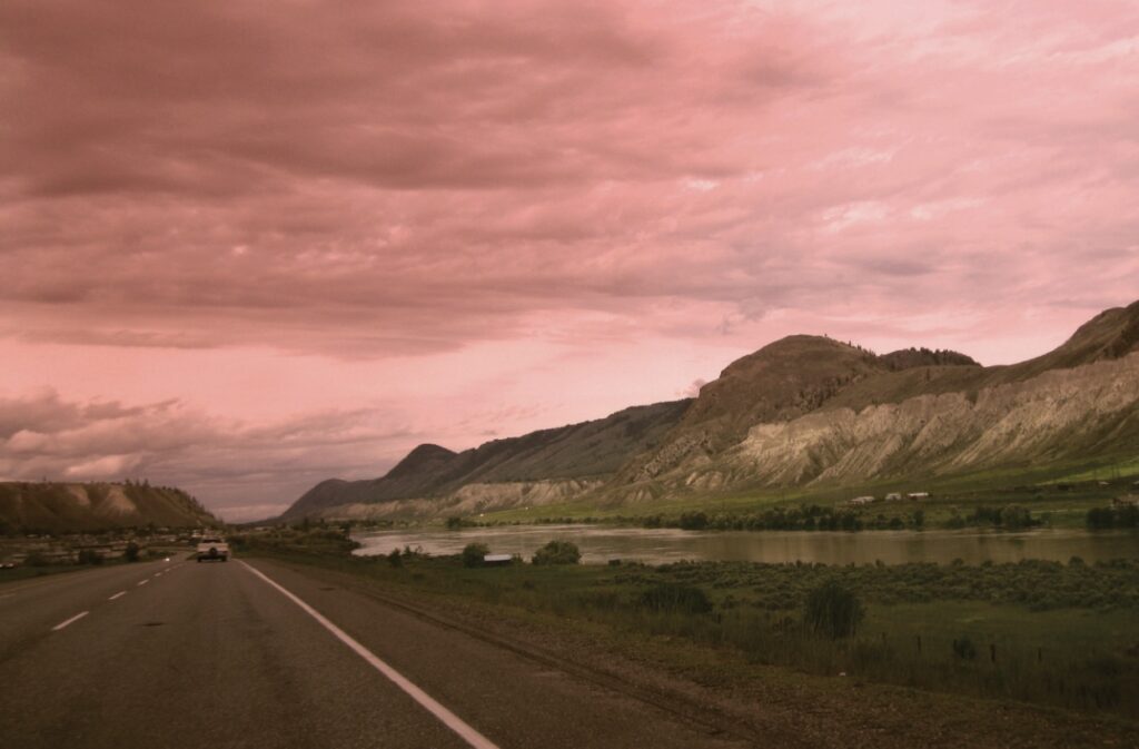 Highway beside river and low arid hills and cloudy sky with truck far ahead. Credit Derek von Essen 