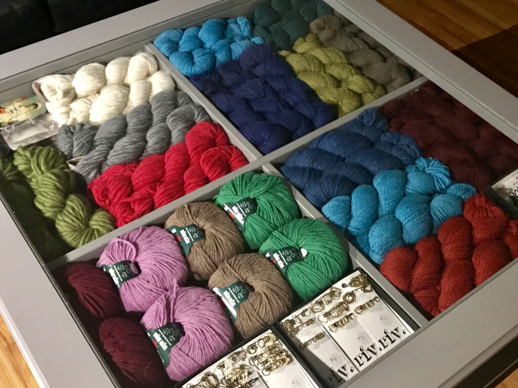 An array of colourful yarns, many in skeins, neatly organized in squared sections of a drawer or other container