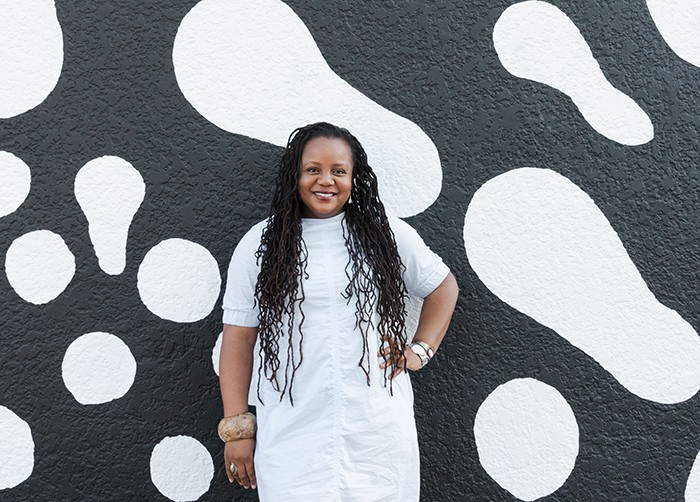 Designer Tafui McLean standing in front of one of her black and white designs wearing a white dress