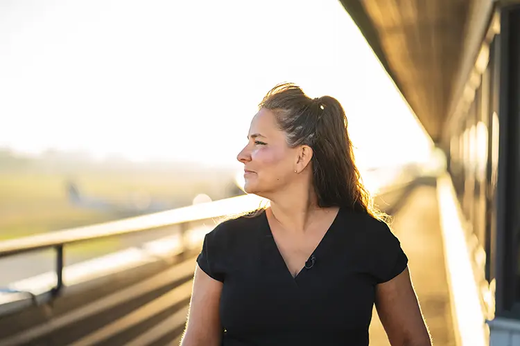 Profile portrait of a woman (pilot Teara Fraser) looking out over her right shoulder with an out of focus structure receding behind her in soft natural light