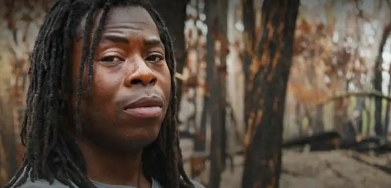 Head and shoulder portrait of Ade Adepitan in a forest in eastern Australia after a devastating bush fire had passed through