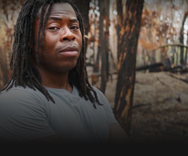 Head and shoulder portrait of Ade Adepitan in a forest in eastern Australia after a devastating bush fire had passed through