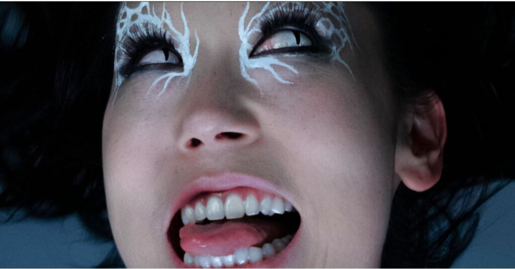 Close-up of woman's face, wild-looking with wavy white makeup around her black-rimmed eyes