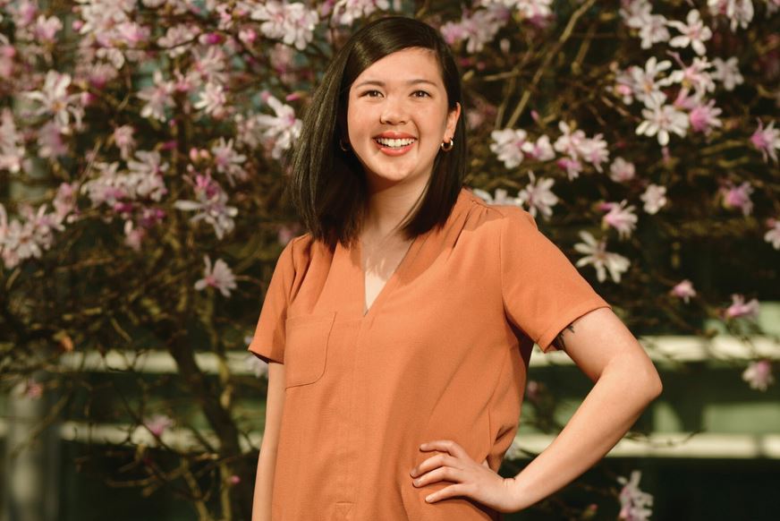 Portrait of young woman (the writer) in a soft orange t-shirt in front of a blooming bush