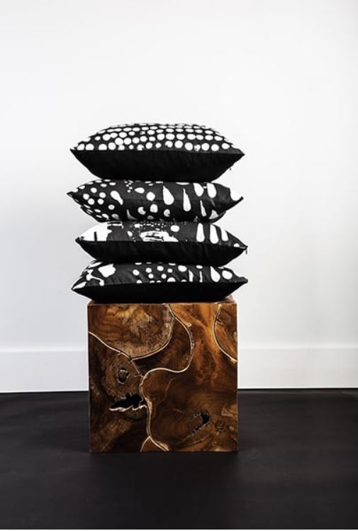 A stack of designer Tafui McLean's black and white pillows on an elaborate square wooden pedestal