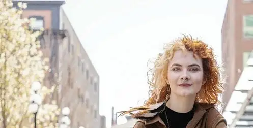Young woman with red hair sitting casually on a ledge with buildings behind her