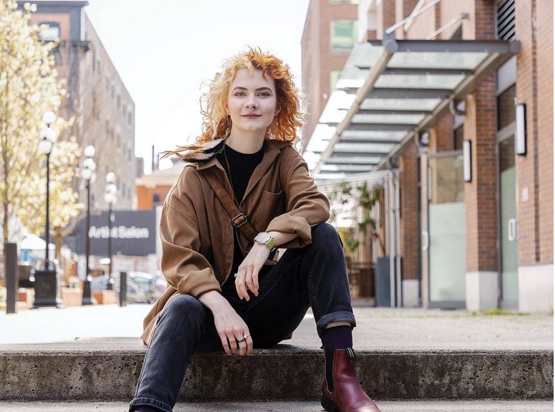 Young woman with red curly hair sitting casually on a top stair in a pedestrian area