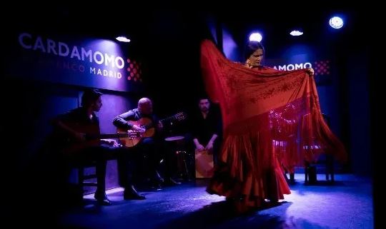 Flamenco dancer Paula Rodriguez in red dress and shawl dancing on stage at Cardamomo, Madridwith musicians in the background