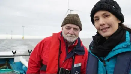 Zoologist George McGavin and oceanologist Helen Czerski aboard a research vessel on the North Sea with a wind farm in the background