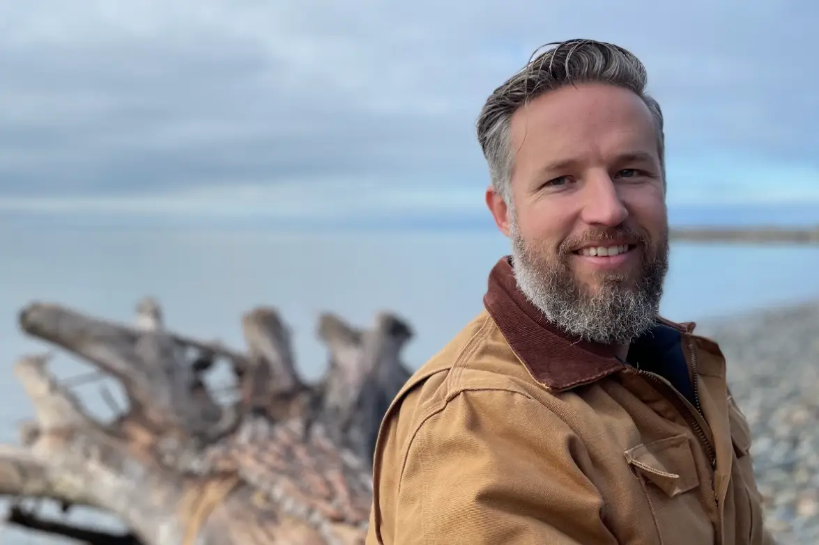 Anthony Robinson on beach in front of tree stump