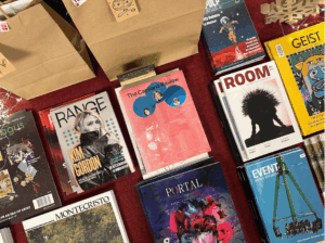 Non-Traditional Newsstand project, section of table set-up at Massey Theatre, New Westminster displaying stacks of MagsBC member magazines.