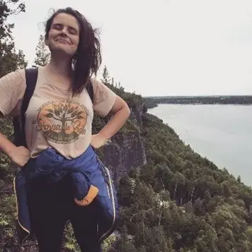 Colour portrait of Jessie Willms standing on a cliff in an outdoor setting with a body of water in the background.