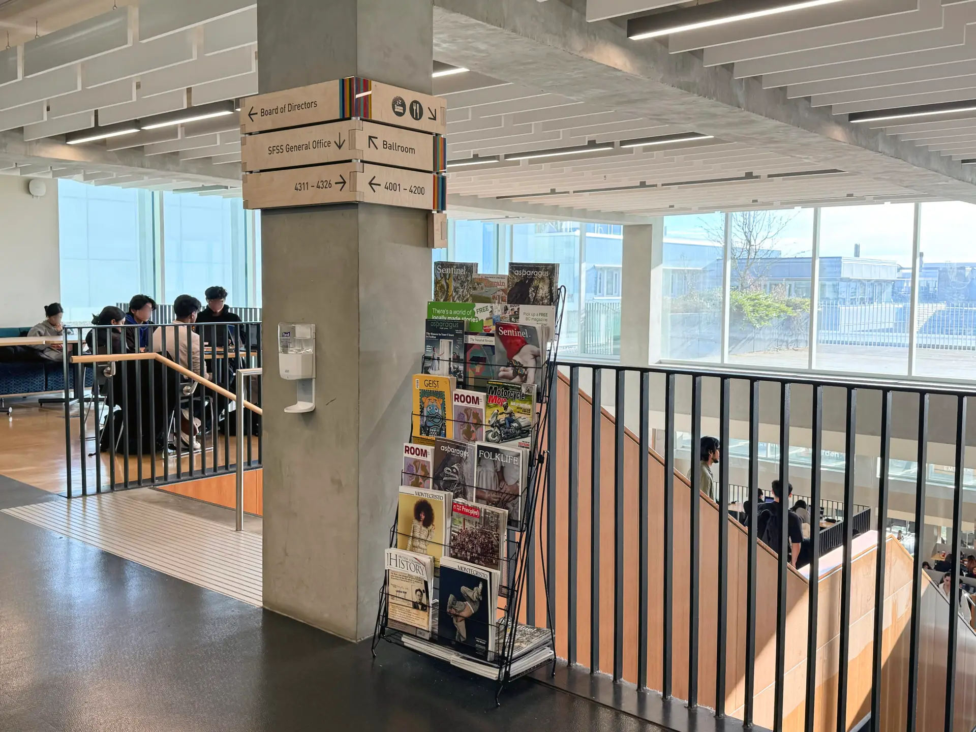 Interior view of the Student Union Building at Simon Fraser University, showing a display of MagsBC member magazines beside a post and above a staircase.