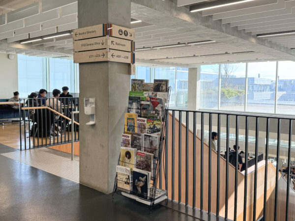 Interior view of the Student Union Building at Simon Fraser University, showing a display of MagsBC member magazines beside a post and above a staircase.