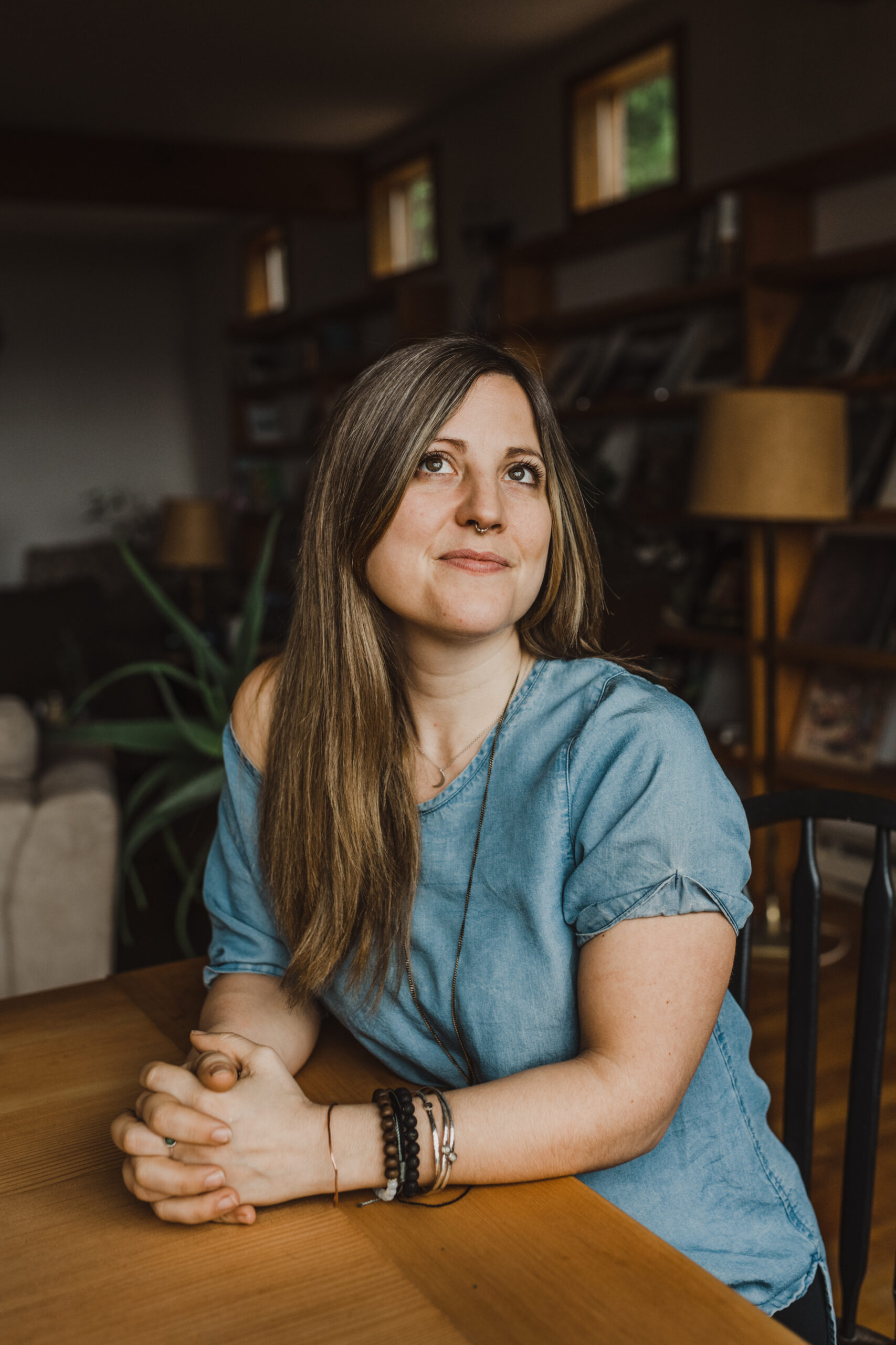 Colour portrait of Alina Cerminara in a domestic interior setting, leaning lightly forward on a table with her arms and hands