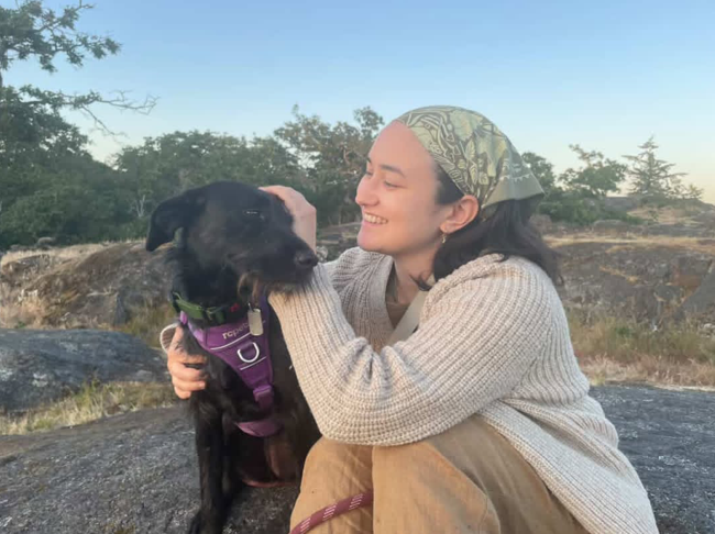 Portrait of L'Amour Lisik with a black dog in an outdoor setting