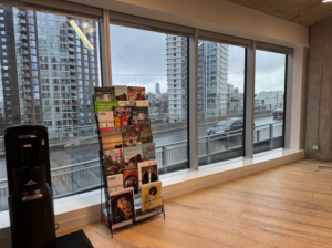 Photo of newsstand against large windows at University Canada West, Vancouver, BC, featuring a variety of BC magazines. Photo by Sun Woo Baik.