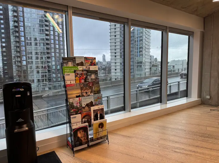 Photo of newsstand against large windows at University Canada West, Vancouver, BC, featuring a variety of BC magazines. Photo by Sun Woo Baik.